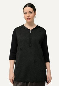 Tunic nera in maglia con chiusura lampo frontale, cappuccio e maniche a tre quarti. Presenta un sottile motivo testurizzato su tutta la superficie.