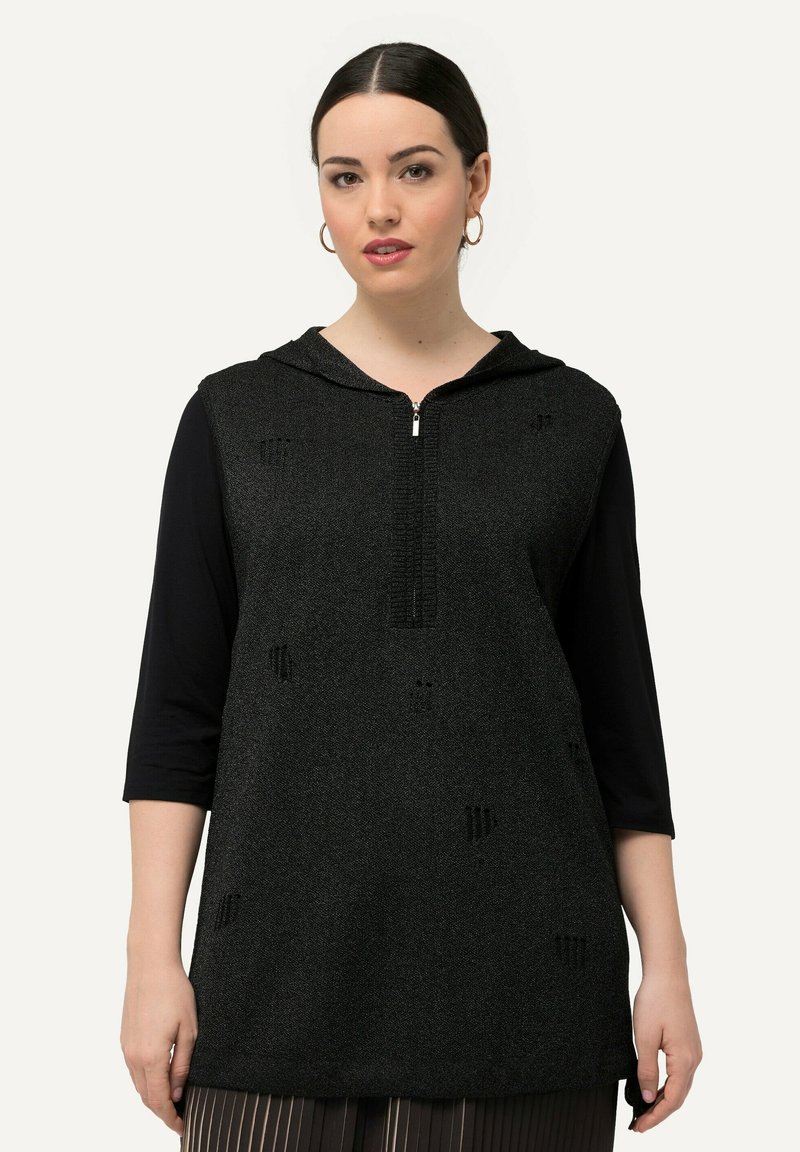 Tunic nera in maglia con chiusura lampo frontale, cappuccio e maniche a tre quarti. Presenta un sottile motivo testurizzato su tutta la superficie.