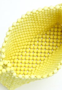 Cesto giallo realizzato con perline rotonde e esagonali, con una superficie texture e una forma curvata. Le perline sono uniformi in dimensioni e colore.