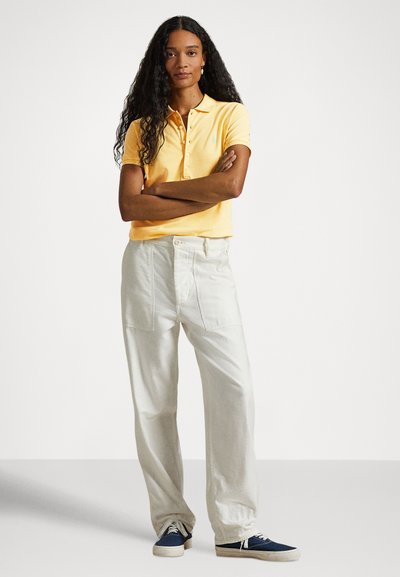 Žlté polo tričko s golierom a gombíkmi, v kombinácii s voľnými, svetlými nohavicami a tmavomodrými teniskami.