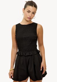 Robe noire sans manches avec un corsage froncé et une taille froncée. La jupe présente un design plissé et une coupe ample, fabriquée en tissu léger.