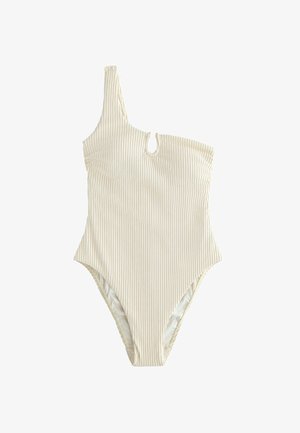 Donna che indossa un costume da bagno bianco monospalla, in piedi all'aperto con gli occhi chiusi e la testa inclinata all'indietro su uno sfondo di cielo azzurro.