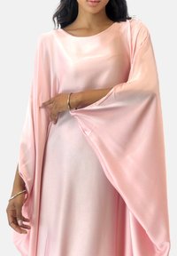Roze satijnen jurk met lange, vloeiende mouwen. Gladde textuur, ronde halslijn en een losse pasvorm. Opvallende zilveren armband om de pols.