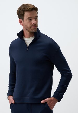 Pullover blu navy con colletto alto e mezza zip, caratterizzato da maniche lunghe e un tessuto morbido e texturizzato. Design semplice, senza motivi.