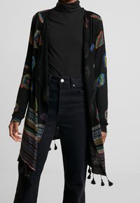 Schwarze Strickjacke mit bunten geometrischen Mustern und Quastenakzenten; leichtes Strickmaterial, offene Vorderseite, lange Ärmel und lässige Passform.