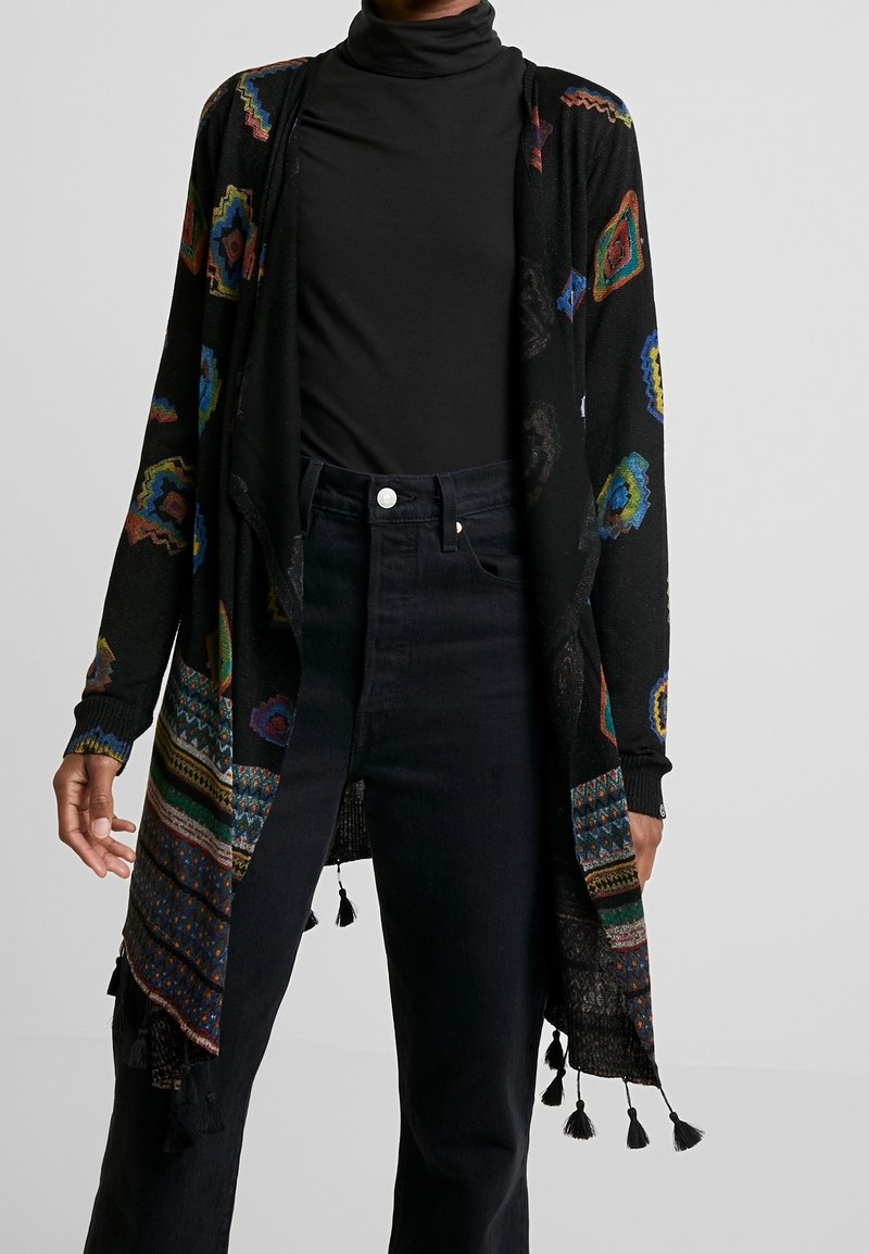 Svart kofta med färgglada geometriska mönster och fransdetaljer; lättstickat material, öppen front, långa ärmar och avslappnad passform.