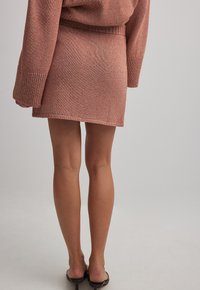 Pleteni mini krilo v teksturirani, topli oranžni barvi z fleksibilnim pasom. Enostaven dizajn, obrobni robovi, v kombinaciji s črnimi čevlji.