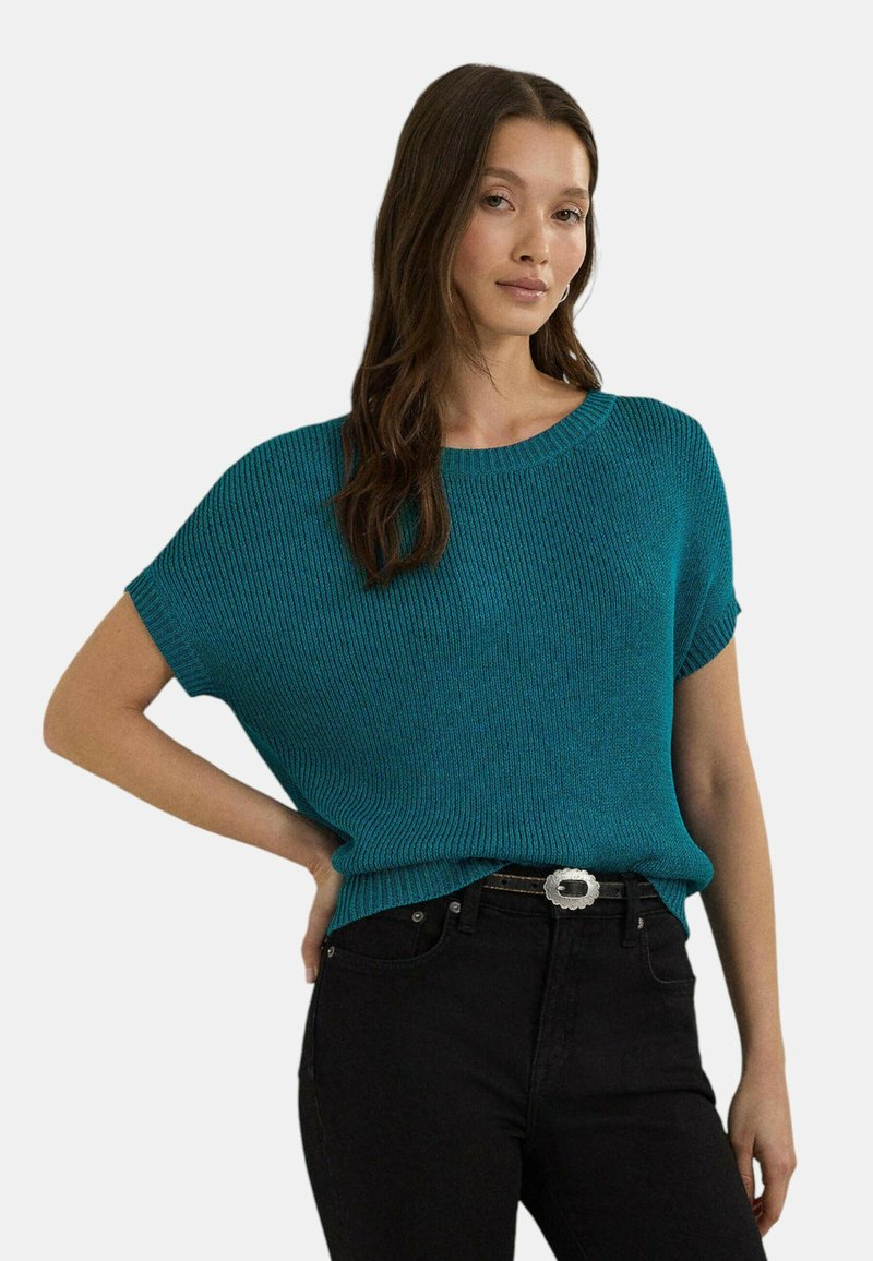 Top in maglia a coste color teal con vestibilità comoda e maniche corte, abbinato a jeans scuri e una cintura con fibbia argentata.