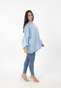 Hellblaues, übergroßes Sweatshirt mit umgeschlagenen Ärmeln, kombiniert mit eng anliegenden blauen Jeans und klaren Blockabsatzsandalen. Sanfte Textur, lockere Passform.