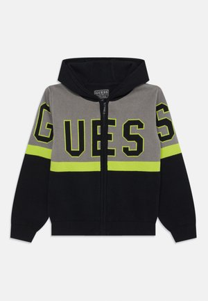 Hooded zip-up jacket in gray, black, and fluorescent yellow. Features large "GUESS" logo and contrasting color blocking. Soft knit material.