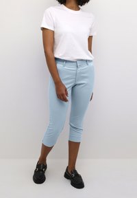 Light blue cropped pants made of stretch fabric, paired with a white t-shirt and black loafers, featuring a smooth texture and tailored fit.