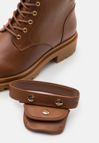 Stivale alla caviglia in pelle marrone con occhielli dorati e una suola spessa e testurizzata, insieme a una pochette in pelle marrone abbinata con hardware dorato.