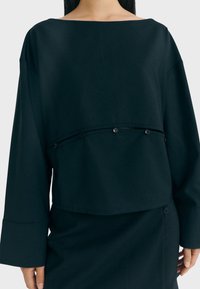 Schwarzes Cropped Top mit einem Bootsausschnitt, weit geschnittenen Ärmeln und einer Knopfdetail an der Taille. Glatte Textur, minimalistisches Design.