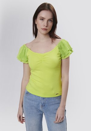 Felgroen top met geplooide korte mouwen, ronde hals en geraffineerd detail aan de voorkant. Draagt met lichtblauwe denim jeans.