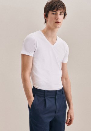 T-shirt en coton blanc à col en V avec des manches courtes, associé à un pantalon tailleur bleu marine, présenté sur un fond neutre.