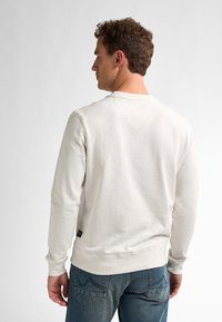 Light beige sweatshirt with a textured finish and speckled pattern, featuring long sleeves and a round neck, paired with blue jeans.