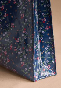 Mėlyna blizgi rankinė su mažais rožiniais, raudonais ir baltais žiedais bei žalių lapų ornamentu, tolygiai išdėstyta visame paviršiuje.