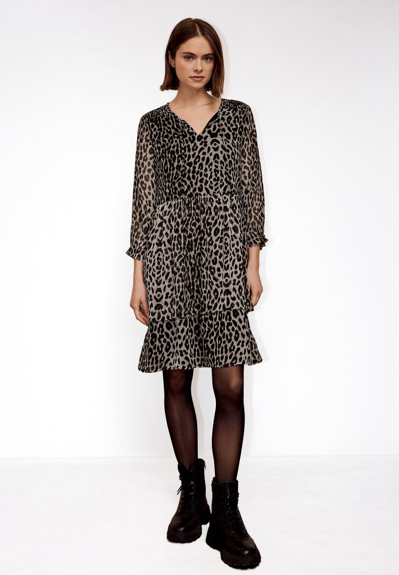 Femme debout portant une robe à manches longues au motif léopard arrivant aux genoux, des collants noirs et des bottes de combat noires à lacets.