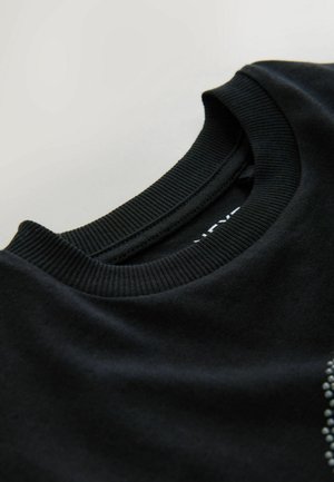 Svart tröja med ribbad rundhals. Slät tyg, har ett subtilt mönster på framsidan och en etikett på baksidan av nacken.