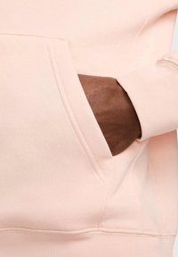 Felpa rosa chiaro con tasca frontale, polsini a costine e una finitura morbida e strutturata. Presenta dettagli di cucitura alle cuciture.