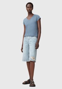 Blå kortærmet V-udskæring top, lyse denim Bermuda shorts med frynset kant og knæslidser, sorte sandaler med stropper og guld accenter.