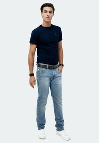 Dunkelblaues, tailliertes T-Shirt, hellblaue Denim-Jeans, schwarzer Gürtel, weiße Sneaker. Slim Fit mit einem dezenten Logo auf der Brust.