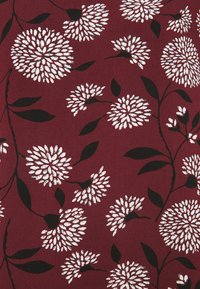 Tessuto maroon con stampa floreale bianca e contorni neri, che presenta forme floreali circolari e foglie verdi, superficie testurizzata.