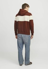 Hoodie w kolorze brązowym i kremowym, z kapturem, wykonany z miękkiego materiału, w zestawieniu z jasnoniebieskimi szerokimi spodniami, które mają tylne kieszenie.