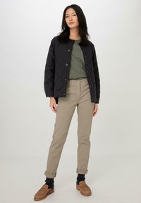 Veste noire matelassée avec un motif texturé, t-shirt vert, pantalon beige clair et mocassins marron, présentés sur un fond neutre.