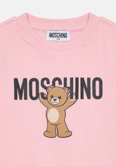 Rózsaszín pamut póló, amelyen egy rajzfilm medvére jellemző grafika található, valamint a "MOSCHINO" felirat vastag fekete betűkkel. Kerek nyakú, bordázott szegéllyel.