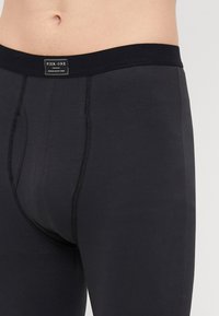 Boxers noirs en mélange de coton avec une large ceinture élastique portant une étiquette de marque, une ouverture à l'avant et une texture lisse.