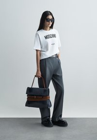 Tricou alb Moschino cu literă neagră, pantaloni gri cu talie înaltă, încălțăminte neagră cu platformă și o geantă mare albastră cu accente maro.