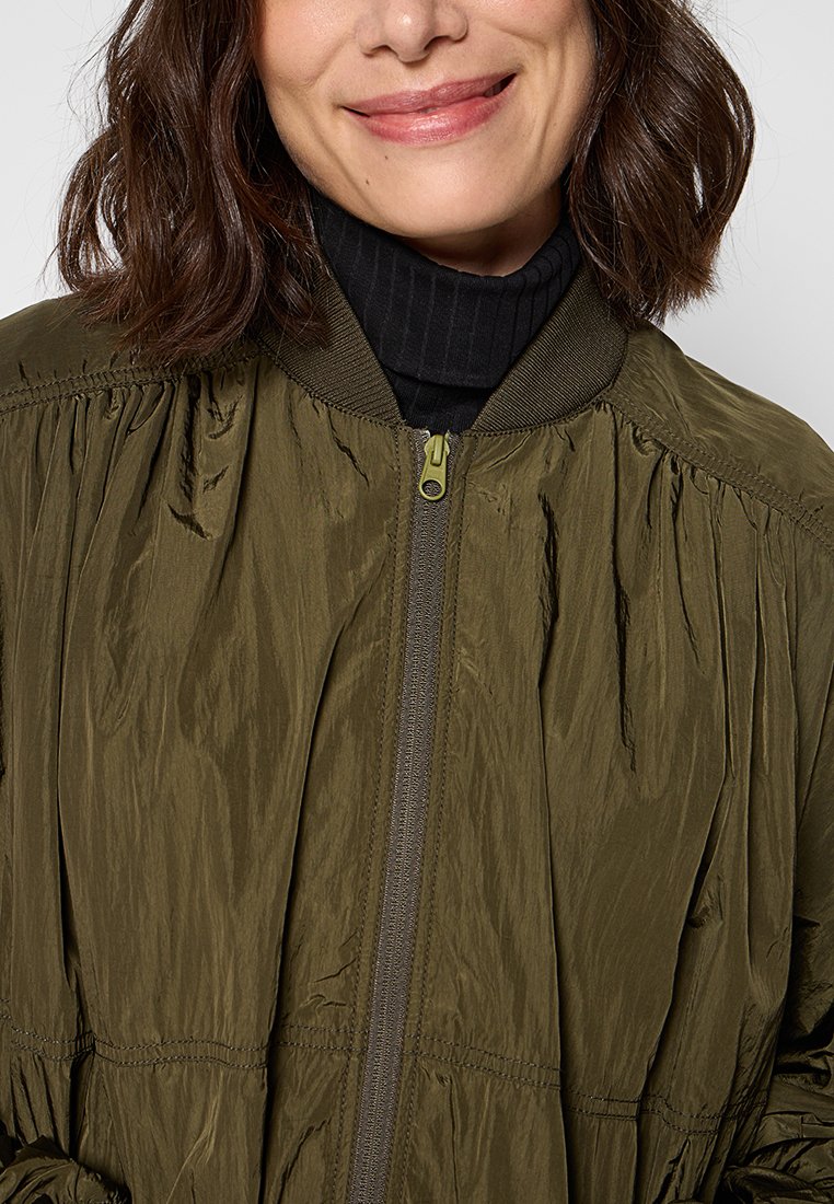Oliwkowa kurtka bomberka z fakturowanej tkaniny, zapięcie na zamek, ściągacz przy kołnierzu oraz marszczenia wzdłuż rękawów i dolnego brzegu.
