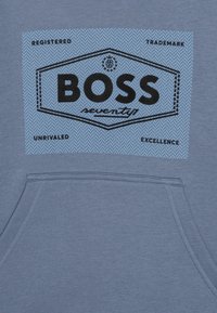 Felpa blu con tasca frontale. Presenta una grande stampa nera "BOSS" su uno sfondo a spina di pesce blu chiaro. Il testo include "REGISTRATO" ed "ECCELLENZA".