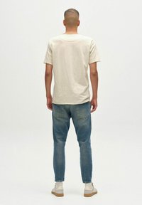 Kremkrāsas kokvilnas T-krekls ar brīvu piegriezumu, apvienots ar ziliem džinsu biksēm. Apavi ir gaiši ar teksturētu zoli. Vienkāršs, ikdienišķs dizains.