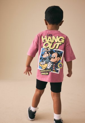 Copil cu fața spre departe, purtând un tricou roz cu desenele animate Mickey, Minnie și Pluto și textul „Hai să stăm de vorbă, trimițând o mulțime de zâmbete.”