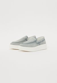 Des chaussures slip-on en suède gris clair avec un bout arrondi, une épaisse semelle en caoutchouc blanc et des coutures minimalistes le long des bords. Texture lisse.