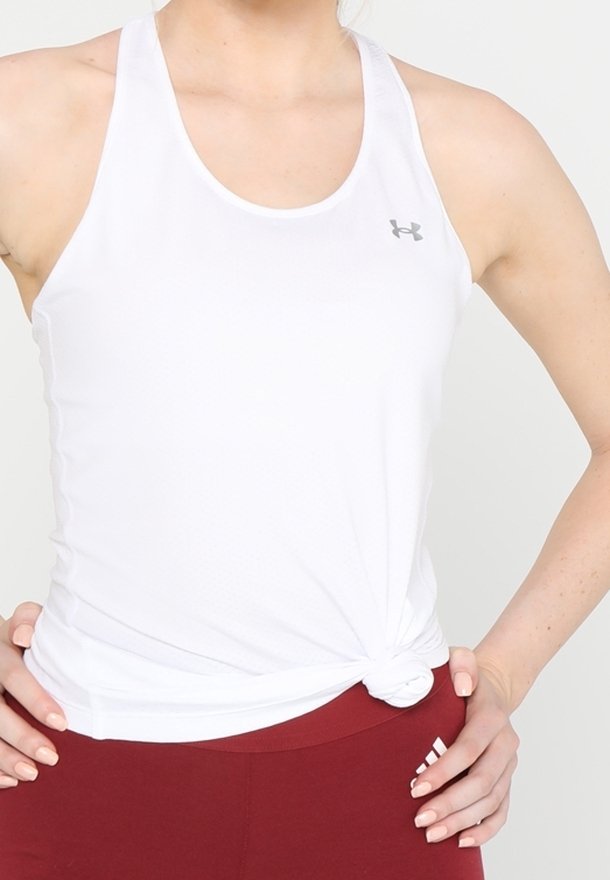 Personne portant un débardeur de sport blanc noué à la taille et un legging de sport rouge avec un logo près de la hanche, mains posées sur les hanches.