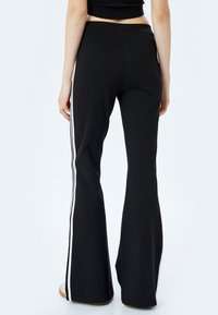 Zwarte flared pantalons met witte zijstreep, gemaakt van rekbaar materiaal. De tailleband is elastisch en biedt een comfortabele pasvorm.