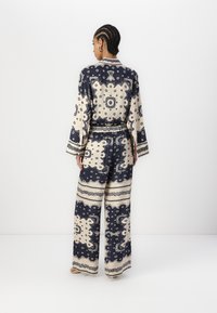 Completo due pezzi a righe blu navy e crema, composto da pantaloni larghi e una maglietta a maniche lunghe, con dettagli intricati e vita decorata da una cintura.