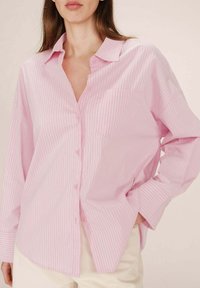 Camicia button-up rosa chiaro con sottili righe bianche, dotata di colletto e una tasca sul petto, realizzata in un tessuto morbido.