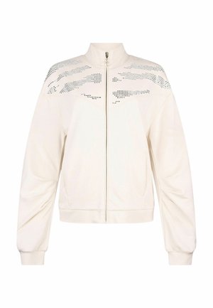 Veste blanche à fermeture éclair avec col montant, manches longues, poignets côtelés et motifs horizontaux argentés cloutés sur le haut de la poitrine et les épaules.