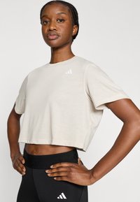 Μπεζ κοντομάνικο αθλητικό μπλουζάκι με κοντά μανίκια και στρογγυλή λαιμόκοψη, με λευκή λεπτομέρεια λογότυπου στο αριστερό στήθος. Ομαλή υφή.