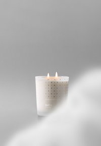 Bougie à deux mèches dans un contenant translucide avec de subtils motifs argentés, étiquetée "Skandinavisk SNÖ Winter Light", projetant une douce lueur sur un fond gris.