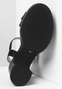 Sandal in pelle nera con tacco a blocco spesso, dotato di suola in gomma texturizzata e cinturino regolabile. Etichetta del produttore visibile sulla soletta.