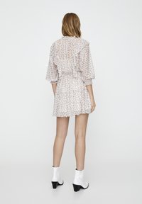 Robe imprimée florale en tissu léger, avec des détails à volants, une taille élastique et des manches longues. Portée avec des bottines blanches.