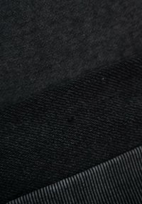 Trzy warstwy materiału w różnych odcieniach czerni: faktura prążkowana, gładka powierzchnia oraz wzór tkany, z każdą o wyraźnie różnym wykończeniu.