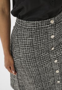 Zwart-wit gestreepte rok van een geweven textuur, met een hoge taille, een a-lijn vorm en zes decoratieve knopen aan de zijkant.