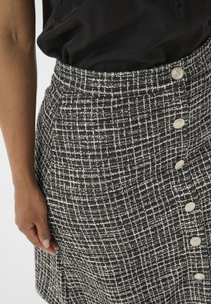 Jupe noire et blanche à motifs dans une texture tissée, présentant une taille haute, une forme évasée et six boutons décoratifs sur le côté.