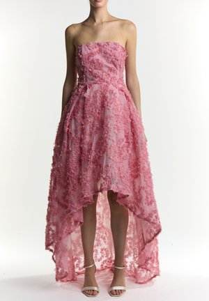 Różowa sukienka bez ramiączek z asymetrycznym dołem, zdobiona teksturowanymi aplikacjami kwiatowymi i przezroczystą warstwą, uzupełniona sandałami na kostkę z paskiem.